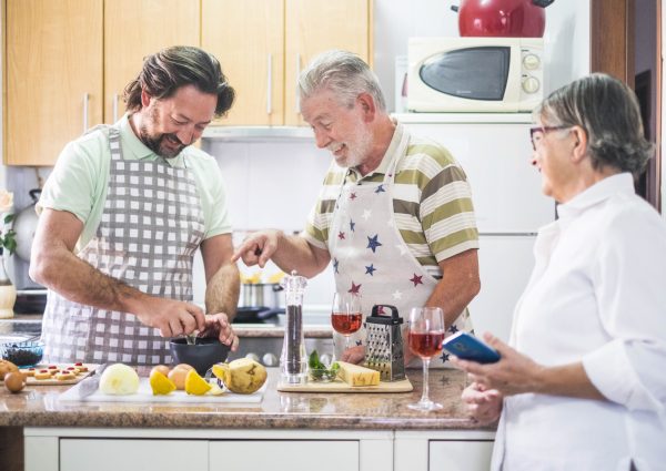 caucasian family three man people cook together lokking the how to do on the mobile phone of the mother. everybody have fun and laugh preparing something to eat. white and bright image