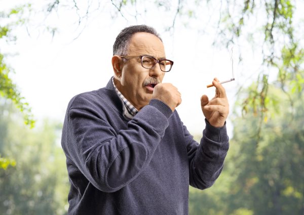 Mature,Man,Smoking,And,Coughing,Outdoors,In,A,Park